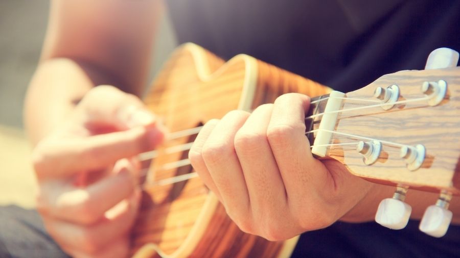 A Man Playing Ukulele on the Sandy Beach in Close up View.