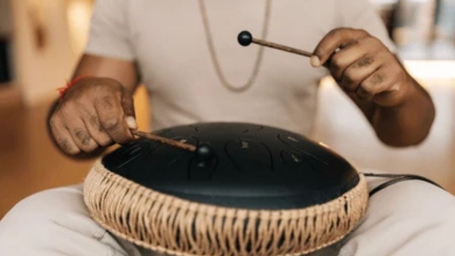 Close-up of a man playing a tongue drum with focused hand movements.