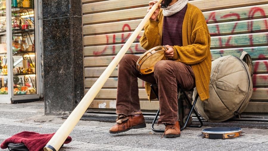 Man sitting down playing a didgeridoo and tambourine