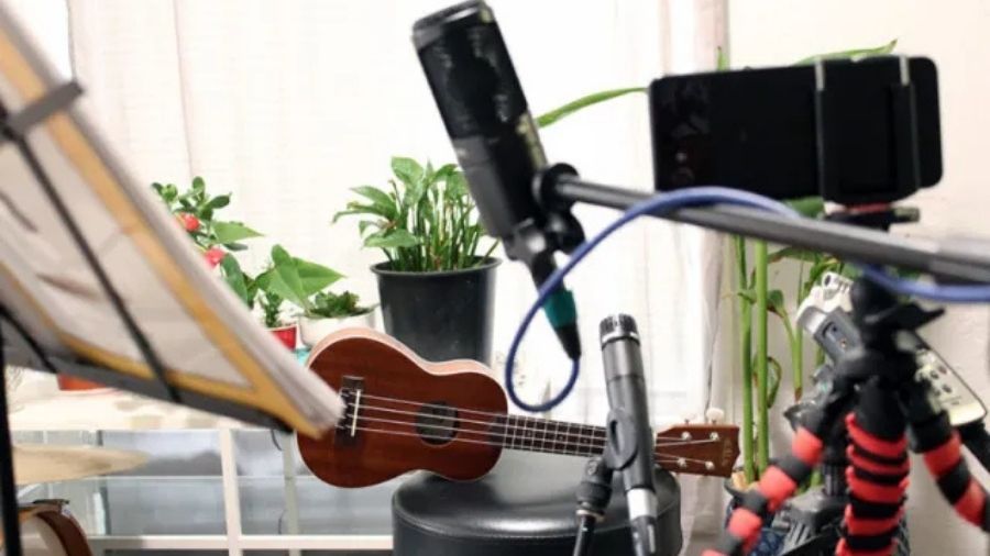 A ukulele in focus on a recording setup, with blurred recording equipment and materials in the background.