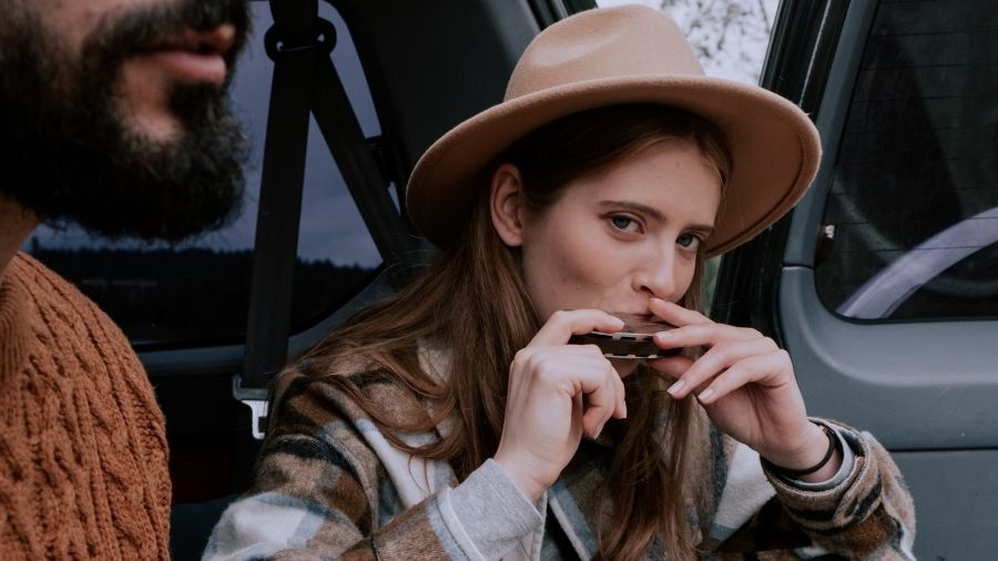 Woman wearing a fedora hat playing a harmonica.”