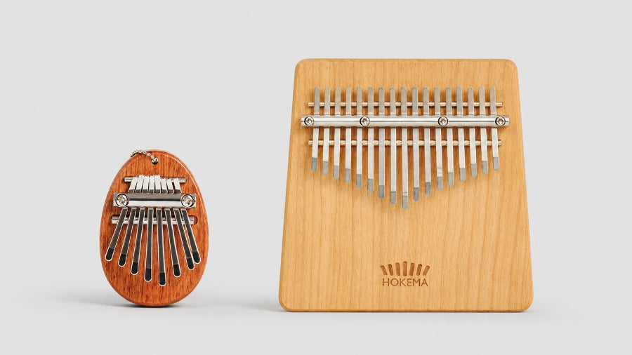 small pocket sized kalimba next to expensive hokema kalimba with 17 notes on a light grey studio background