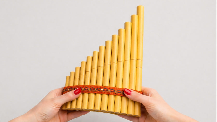 Womens hands holding bamboo siku panpipes on a light grey studio background
