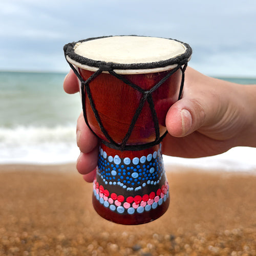 Hand holding a colorful drum on a beach with ocean in the background