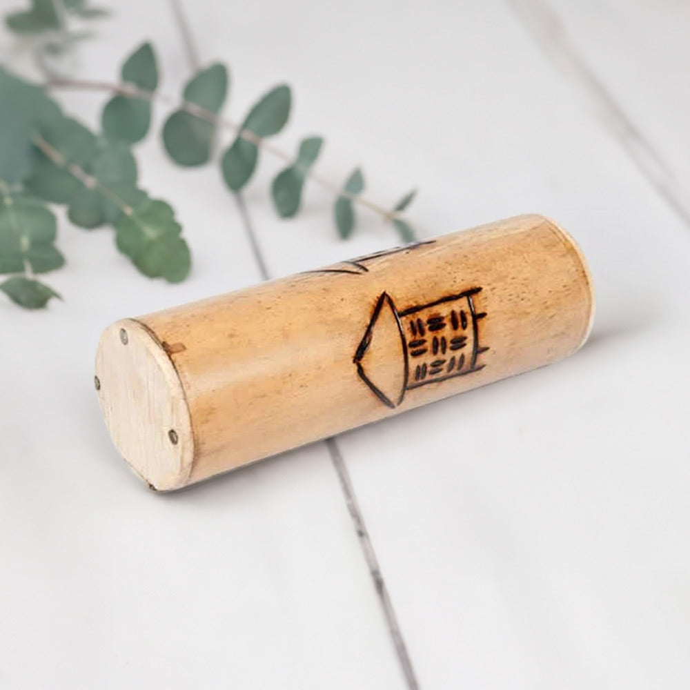 Bamboo Jati Shaker tubular percussion instrument with house carving on white background with eucalyptus stalks