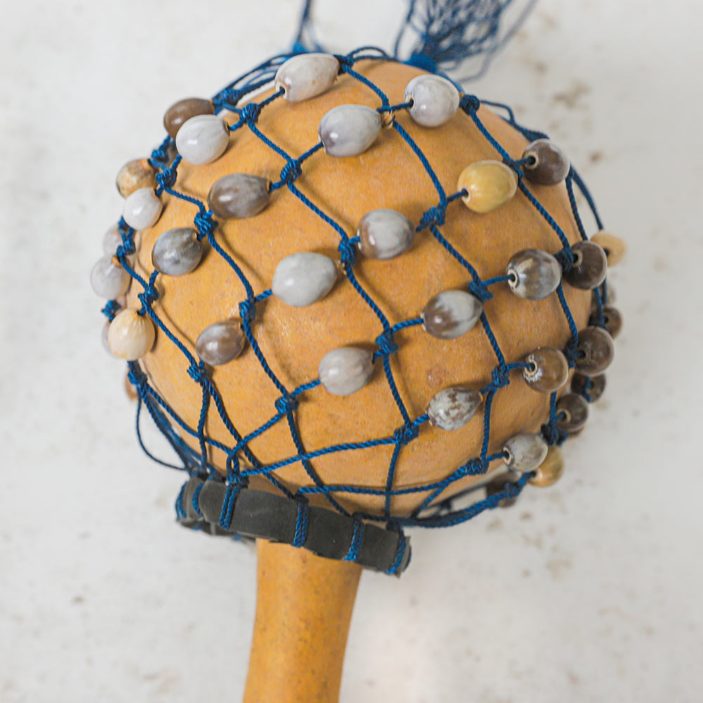 Close up of the small african gourd cabasa shaker percussion instrument showing the natural seeds and beads attached to a net