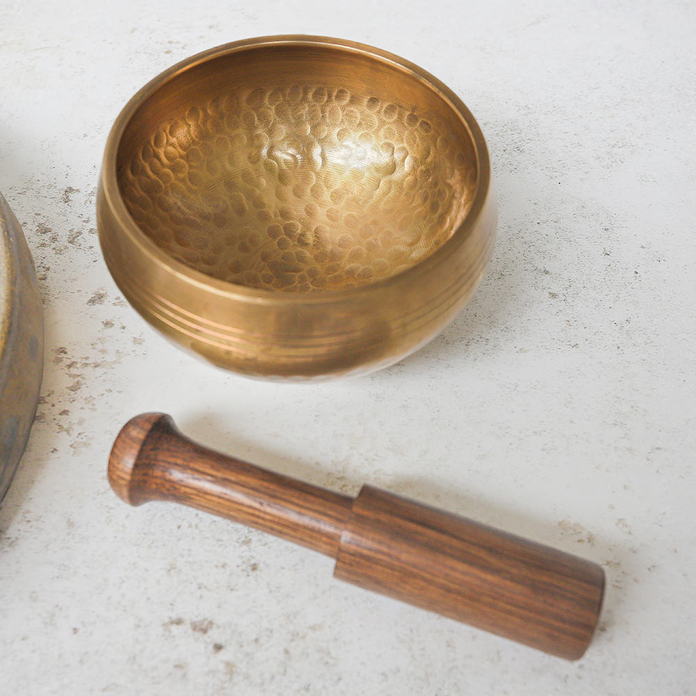 Singing bowl with wooden striker on a textured surface