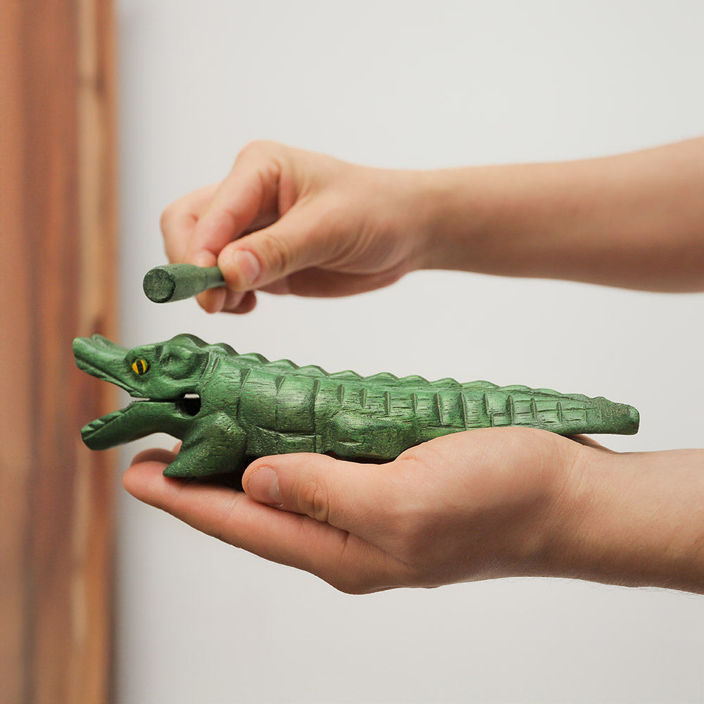 Handheld wooden green crocodile guiro ornament instrument, shown in hand for scale.