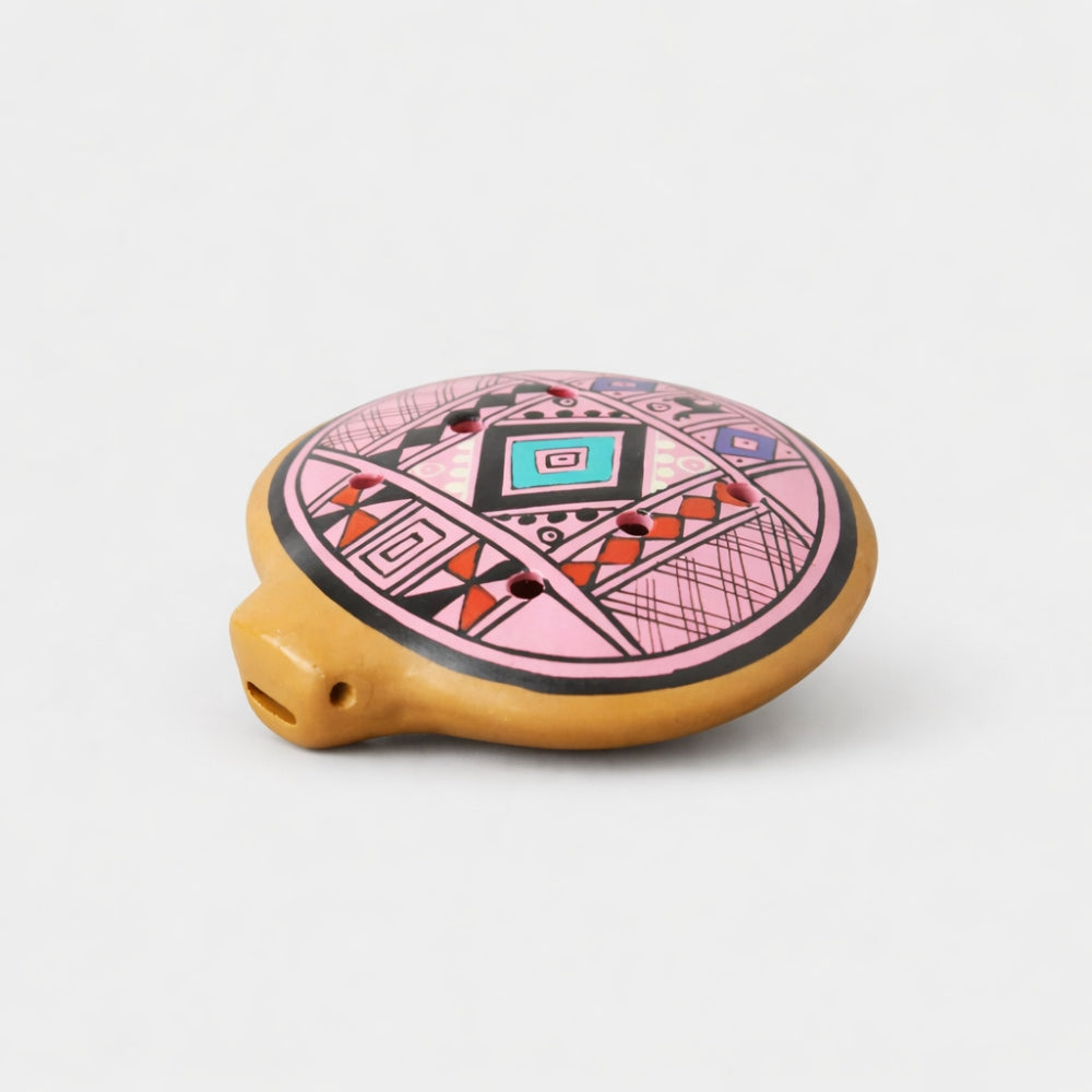 Decorative pink clay ocarina with geometric patterns on a white studio background