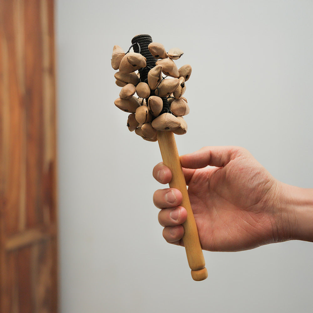 Kenari rattle held in hand, demonstrating its size and natural seed construction.