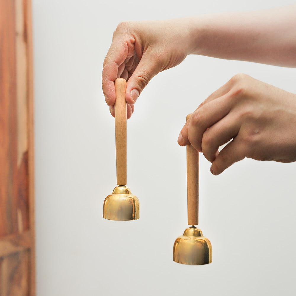Matsu brass bells with wooden handle held in hand, showing the size and design of the instrument.