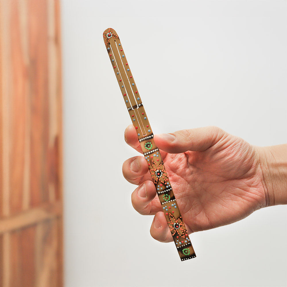 Painted Karinding jaw harp held in hand, demonstrating its size and intricate design.