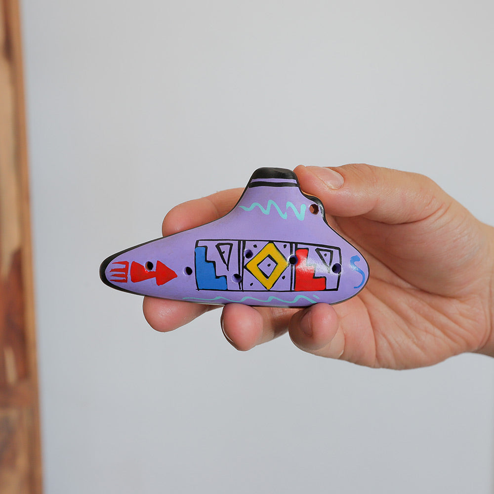 Purple Hand Painted Clay ocarina with geometric designs held in the hand to show scale size.