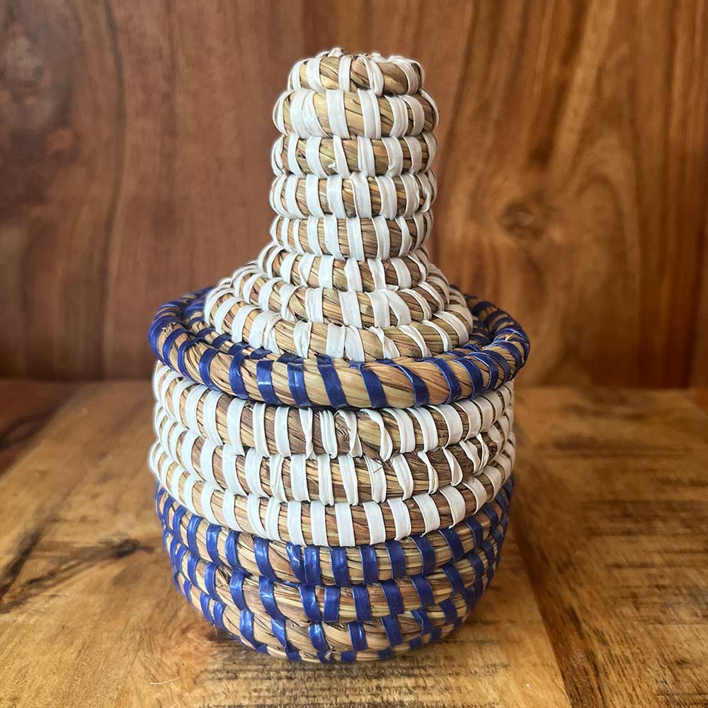A small, handwoven African basket in blue and white, made from straw and recycled plastic, with a matching lid.