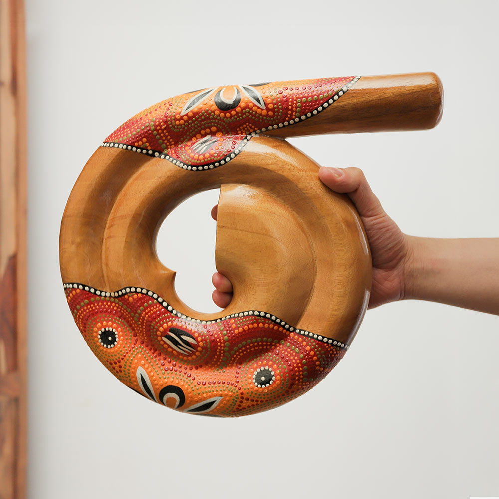 Handheld spiral dot-painted didgeridoo from Indonesia, featuring a red and orange sunburst design