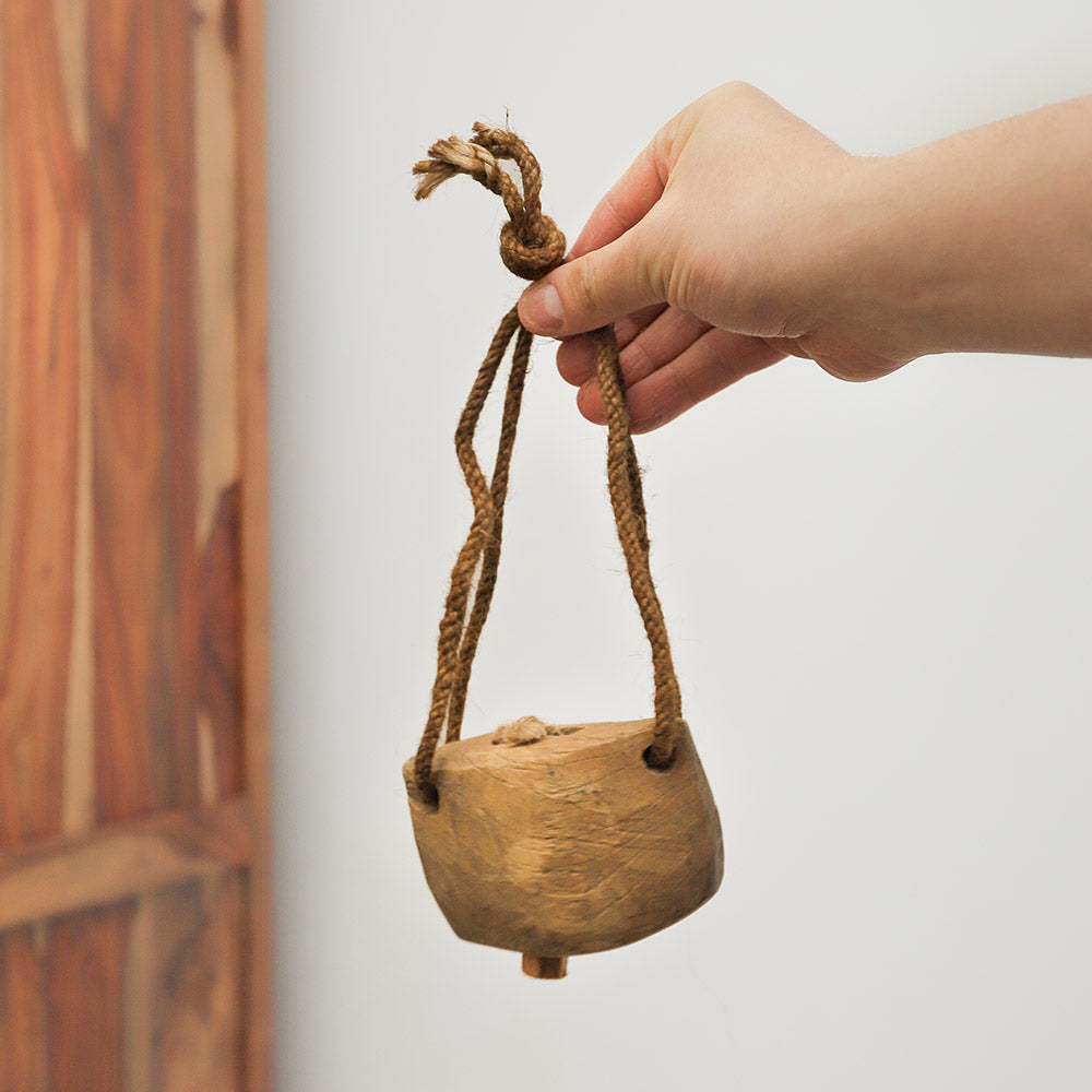 Wooden cowbell hanging from jute string held in hand to show scale and size of the instrument.