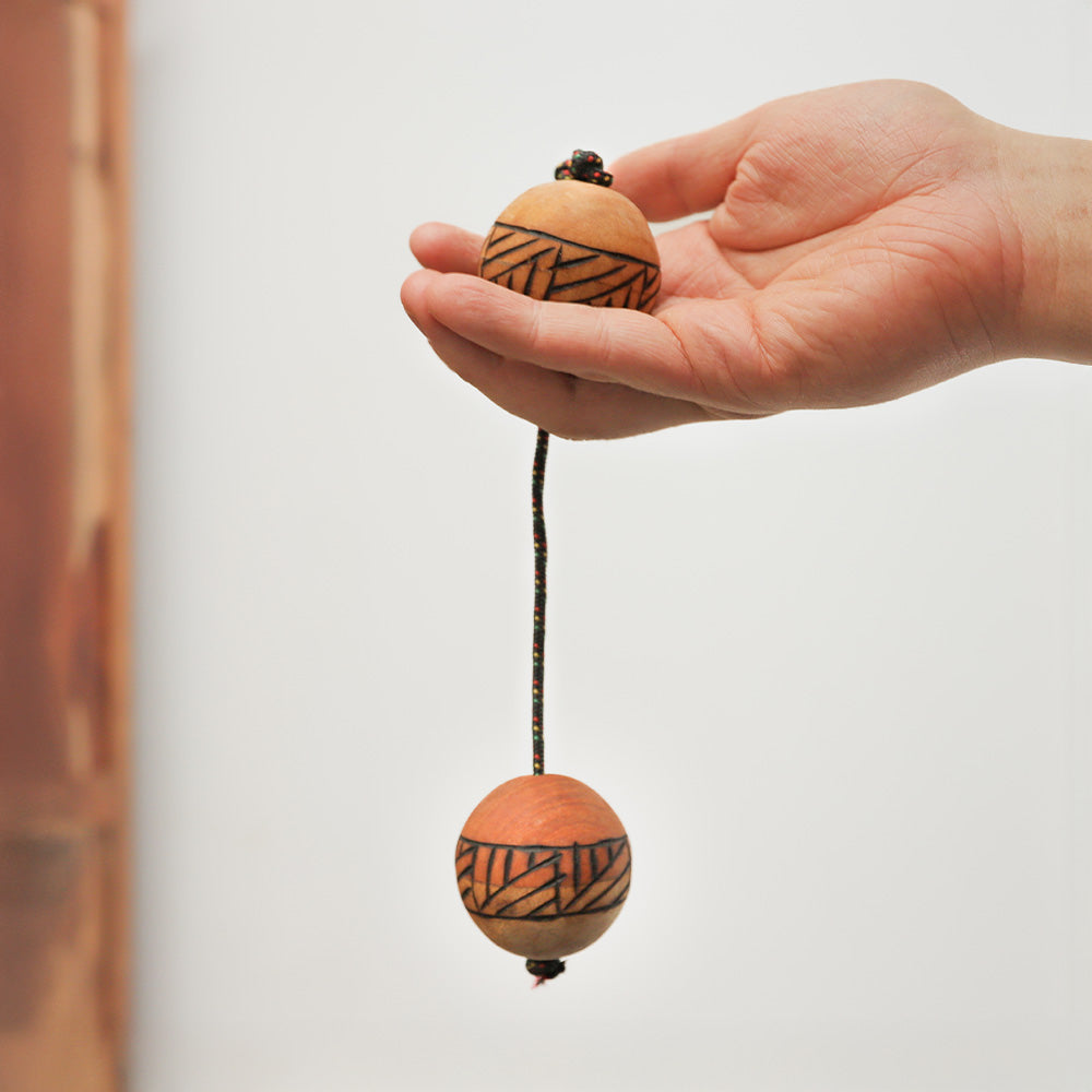 Close-up of a wooden Kashaka shaker with a geometric design, hanging to show scale.