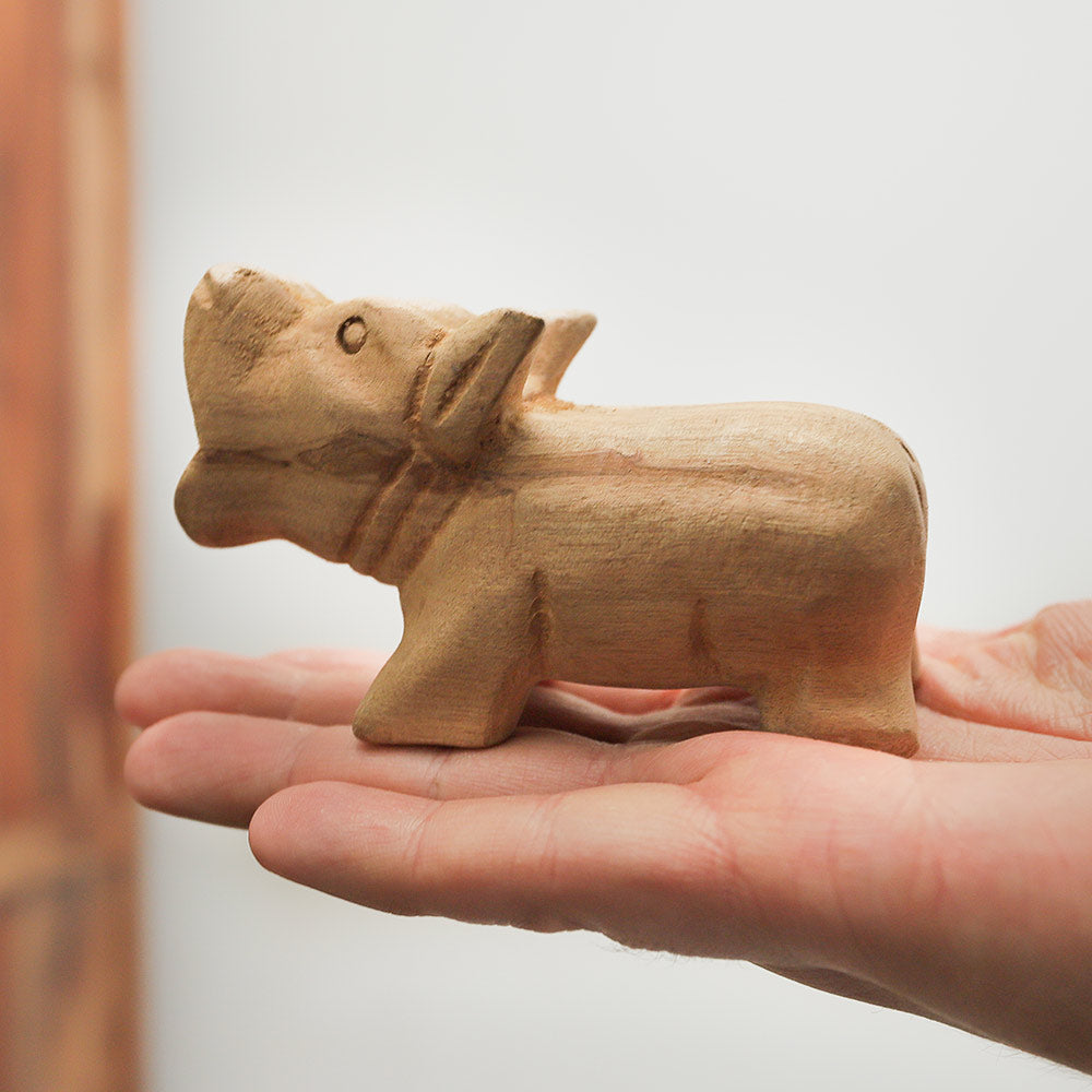 Wooden pig whistle held in hand, demonstrating its size and design.