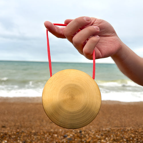 Hand holding a golen gong with a red string on a beach