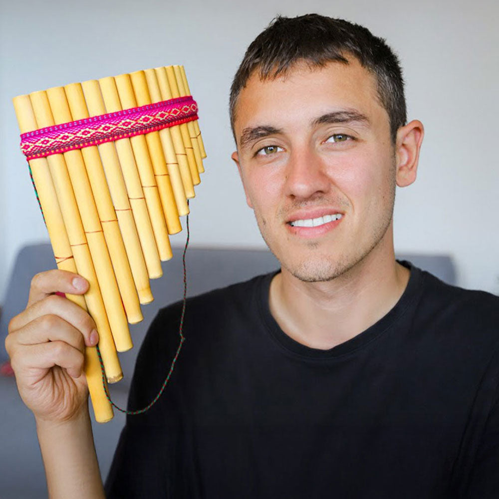 Man holding a pan flute with a colorful band against a plain background
