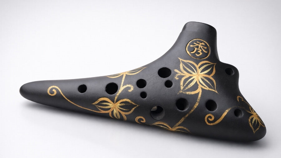 Black ocarina with gold floral design on a clean silver grey studio background