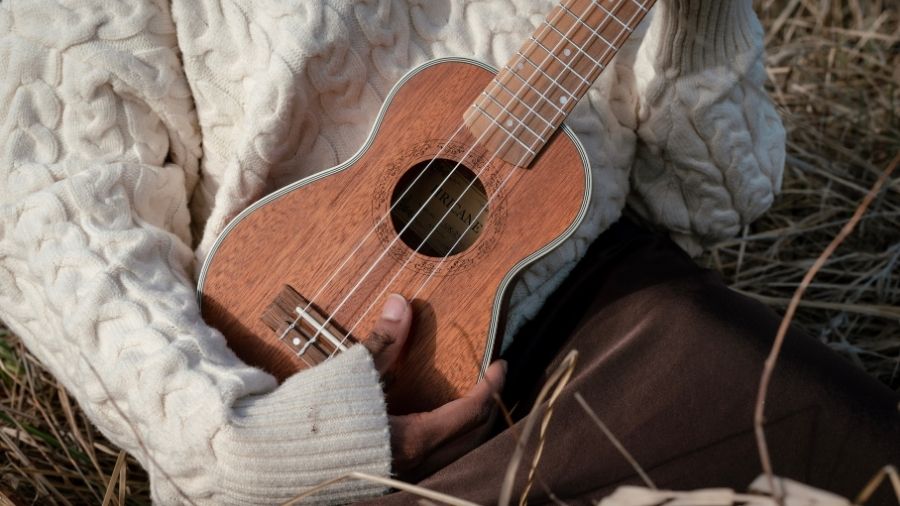 Close-up of a person holding a ukulele, showing their hands and part of the instrument.
