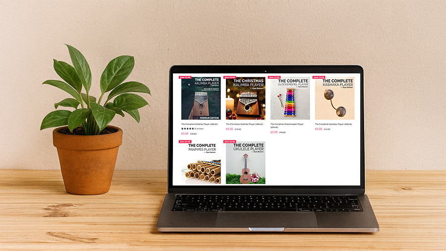Laptop displaying a collection of music eBooks beside a green plant on a wooden desk.