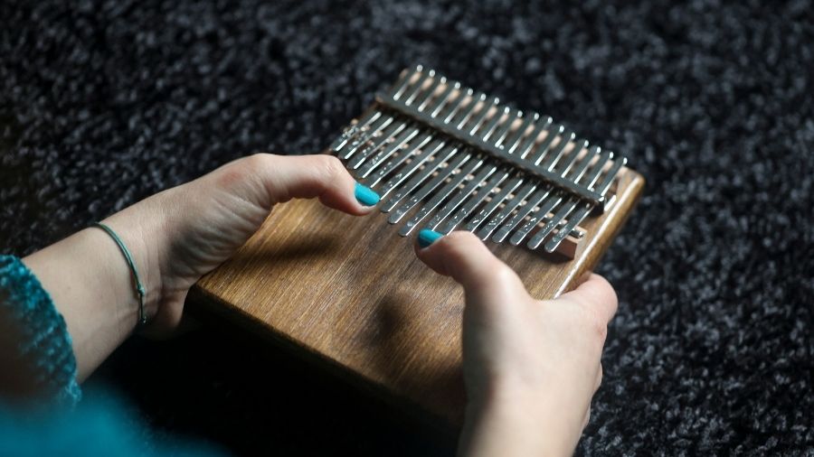 A girl playing a thumb piano, focusing on her hands and the instrument’s metal tines.