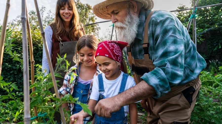 A grandfather teaching his granddaughters about sustainable agriculture outdoors.
