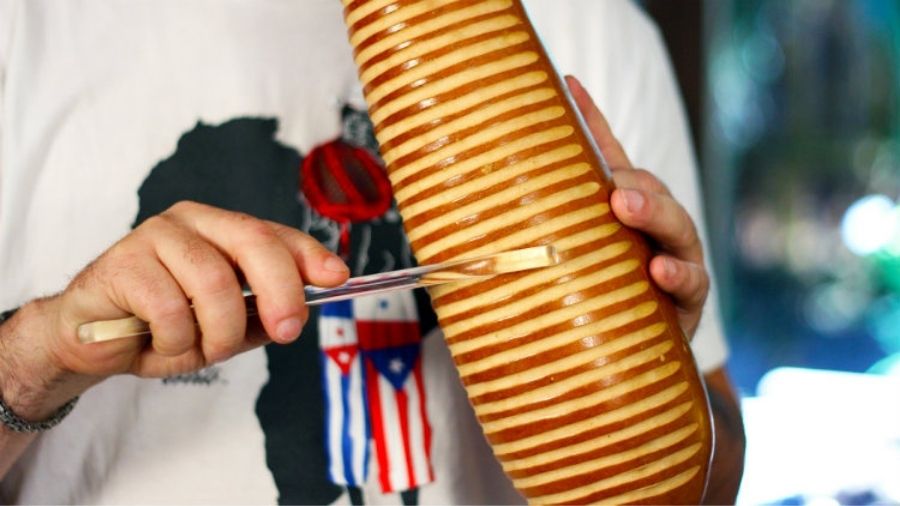 A man holding a guiro and scraping it to produce rhythmic sounds.