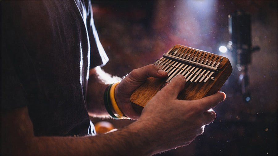 Close-up of a person playing a kalimba, showing hands plucking the metal tines of a wooden thumb piano during a folk music performance