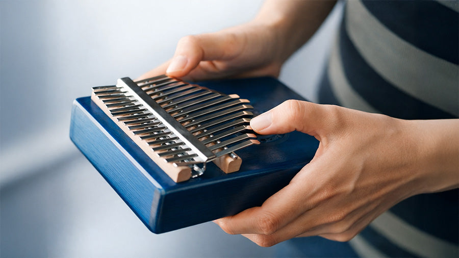 Hands playing chords on a kalimba, showing beginner thumb technique and how to press multiple tines at once