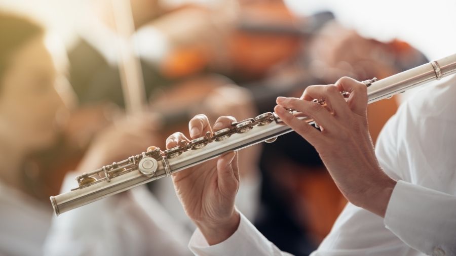 A professional flute player performing on stage, holding the flute in proper playing posture under focused lighting.