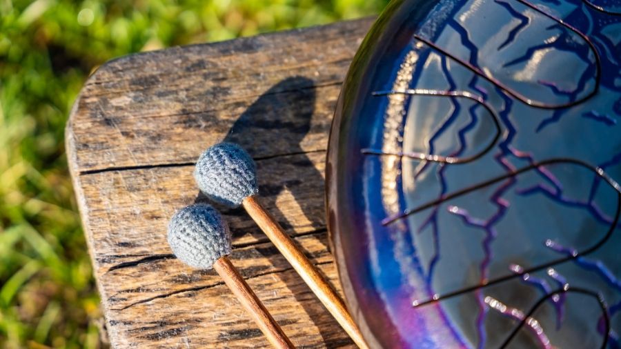Steel tongue drum and mallets resting on a wooden bench, evoking sacred stillness, sound meditation, and harmony with nature.