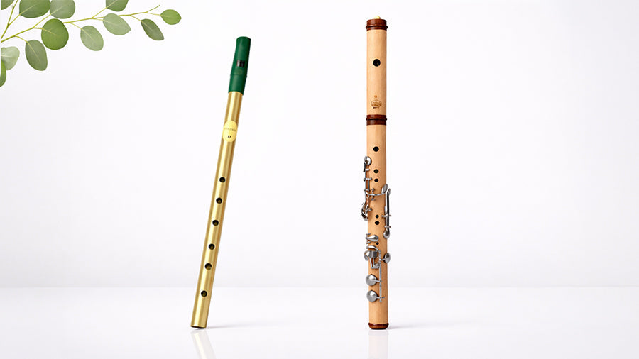 Brass tin whistle and wooden Irish flute displayed side by side on a clean white studio background, comparing traditional Irish woodwind instruments with a minimalist, modern aesthetic.