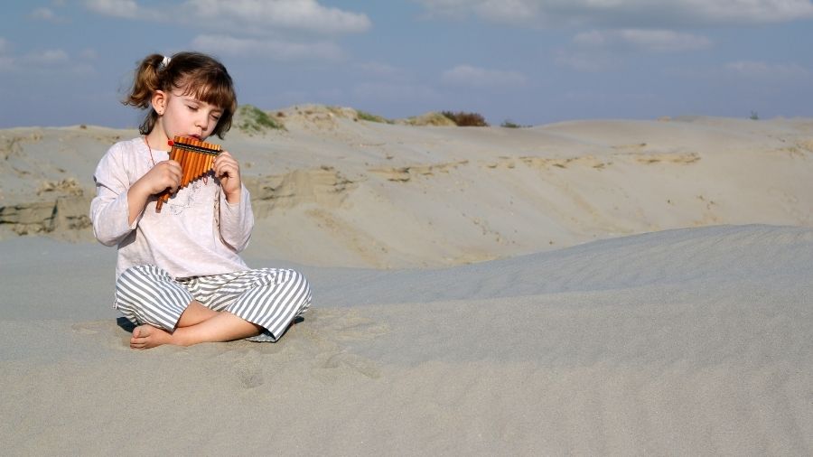 Little girl playing a panpipe in the desert.