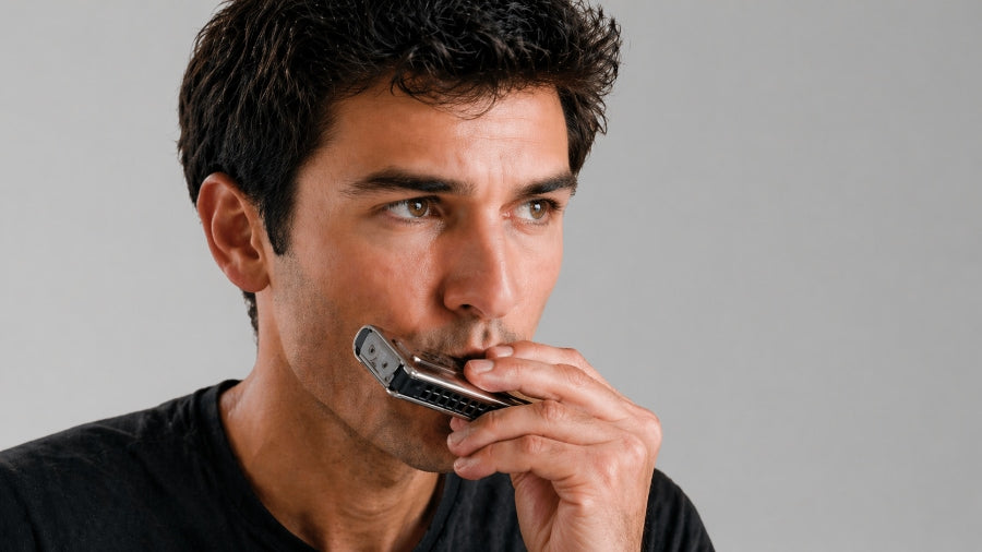 Groomed man playing a harmonica doing a bend technique on a light grey studio background