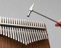 Close up of womens hand holding a tuning hammer and a 21 key kalimba on a light grey studio background