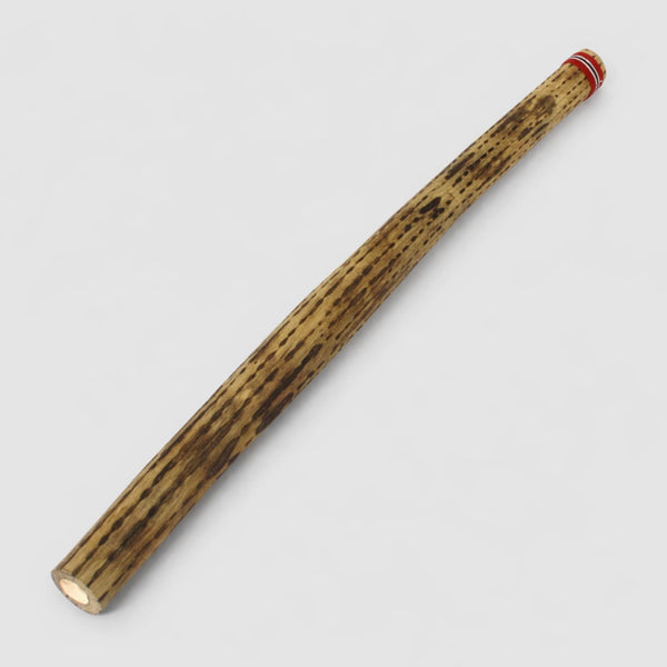 Large 100cm cylindrical cactus rainstick made from deadwood with a colourful red striped woven band on the end on a light gray studio background