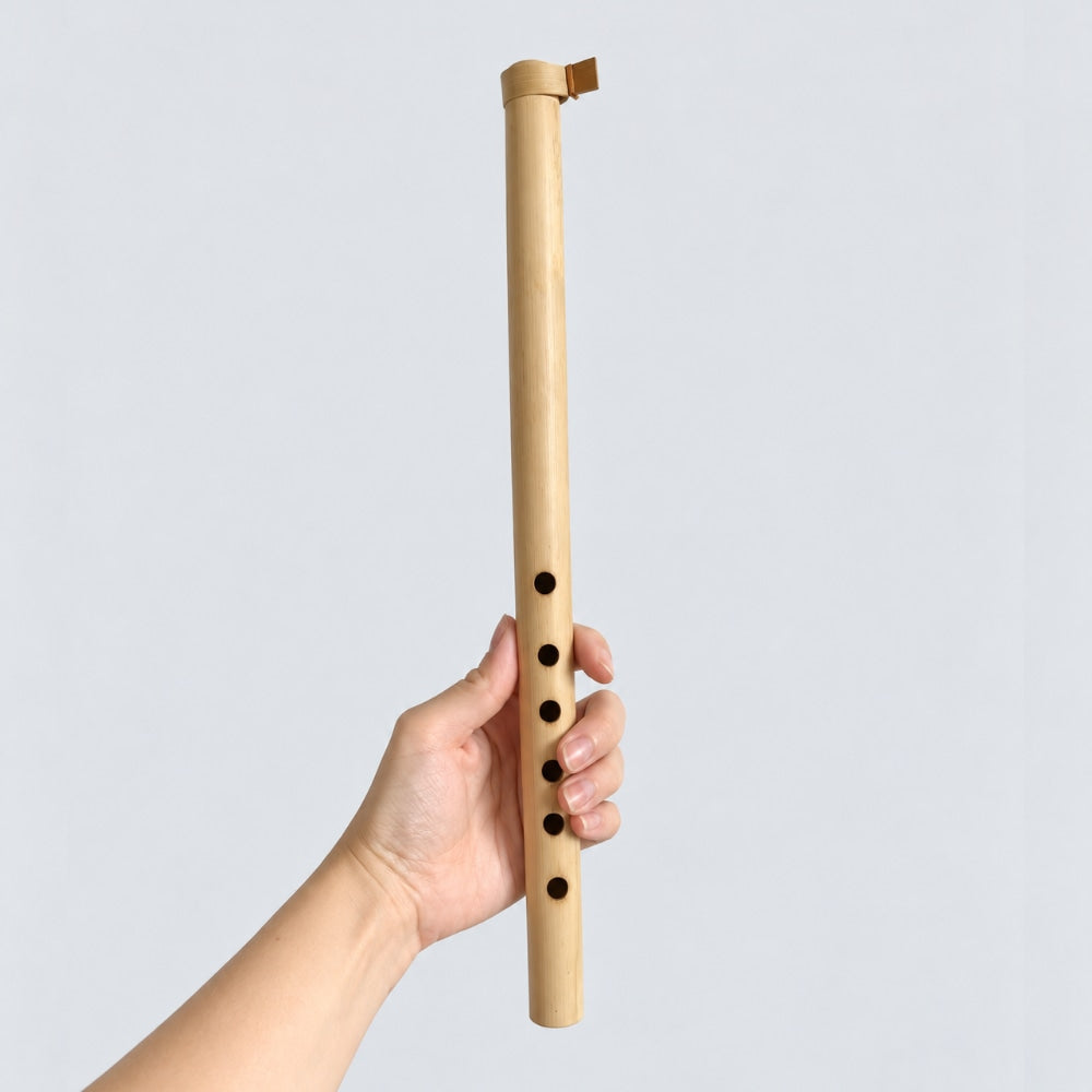 A hand holding a light natural wood flute against a plain light gray background.