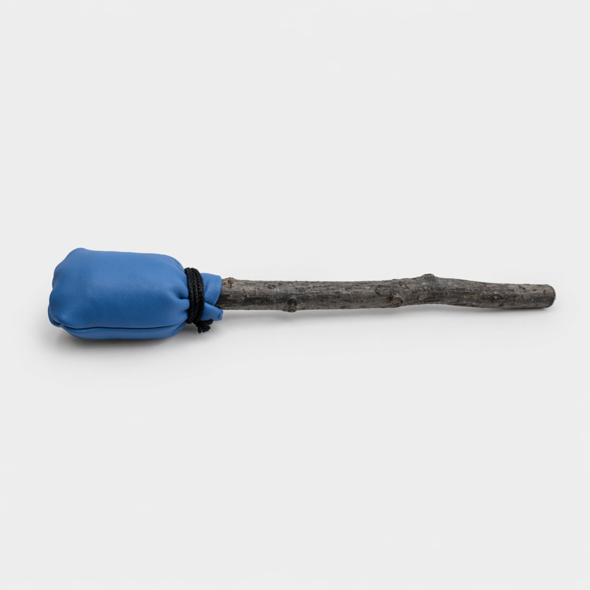 Dark blue shamanic drum beater with wooden stick handle on a light grey studio background