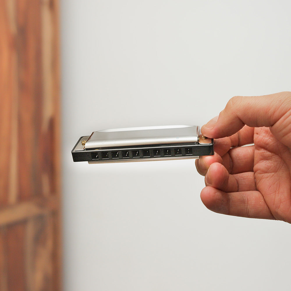 Metal diatonic harmonica held in hand to show size and scale.