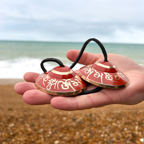Red and gold handbell objects held in a hand with a beach background