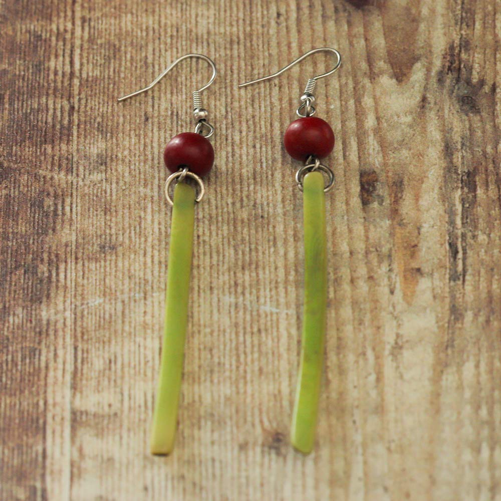 Green and red Tagua earrings on a wooden backdrop