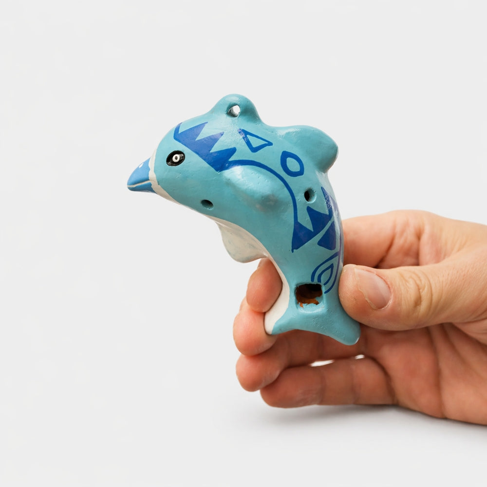 Hand holding a blue dolphin-shaped ocarina against a white background