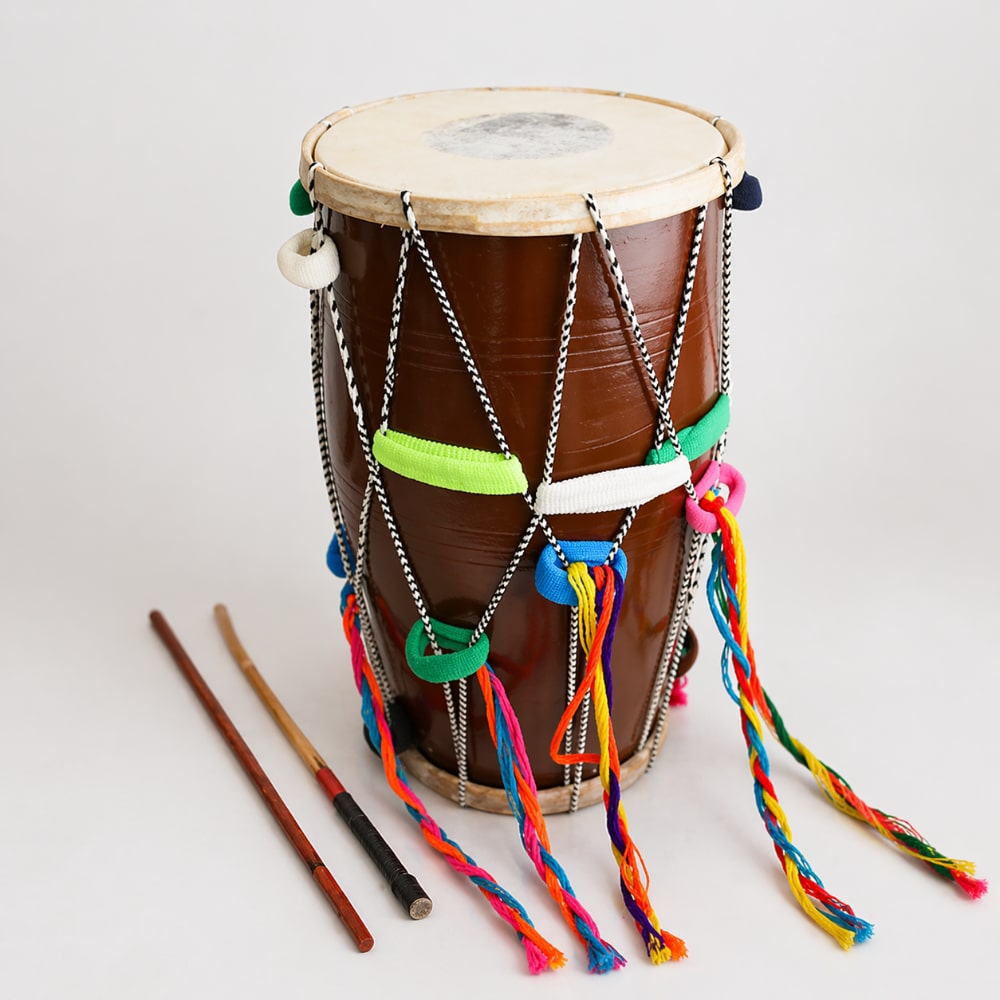 Brown drum with colorful strings and two drumsticks on a light gray background