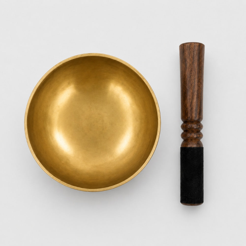 Overhead view of our largest hand beaten brass singing bowl with wooden mallet striker on a light grey studio background