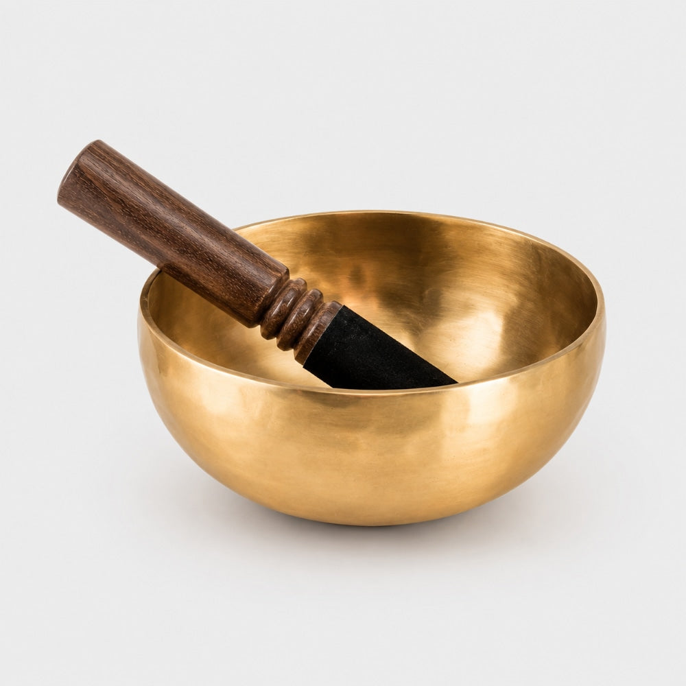 Hand beaten brass singing bowl with natural dark brown wooden beater stick on a light grey studio background