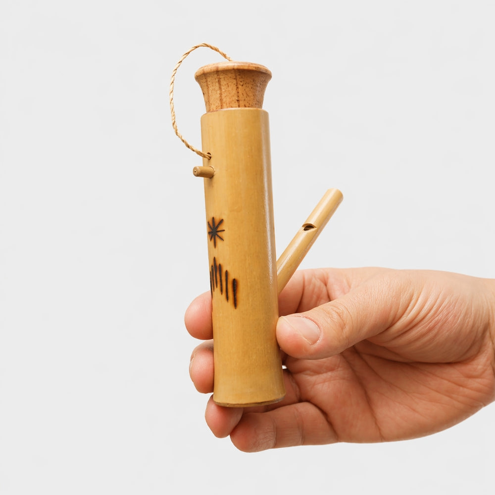 Hand holding a bamboo bird flute with a decorative design on a light gray background