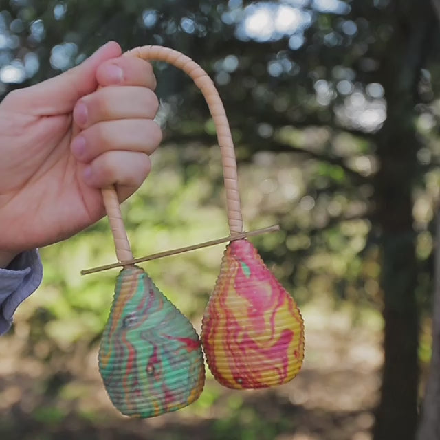 A video of the Double Pesona shaker being played outdoors, showcasing its rhythmic sound in a natural environment.